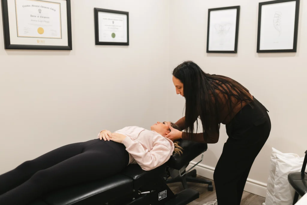 A woman receives treatment from a chiropractor on a therapy table in a room with framed certificates on the wall.