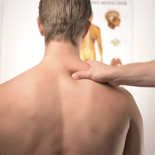 A person receiving a shoulder examination with anatomical posters in the background.